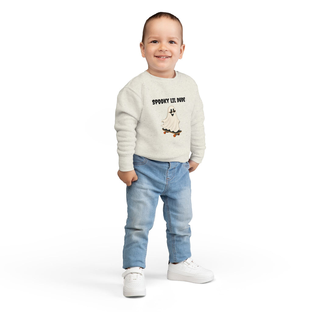 Toddler wearing a beige Spooky Lil Dude Halloween sweater featuring a cute ghost riding a skateboard, styled with casual jeans.