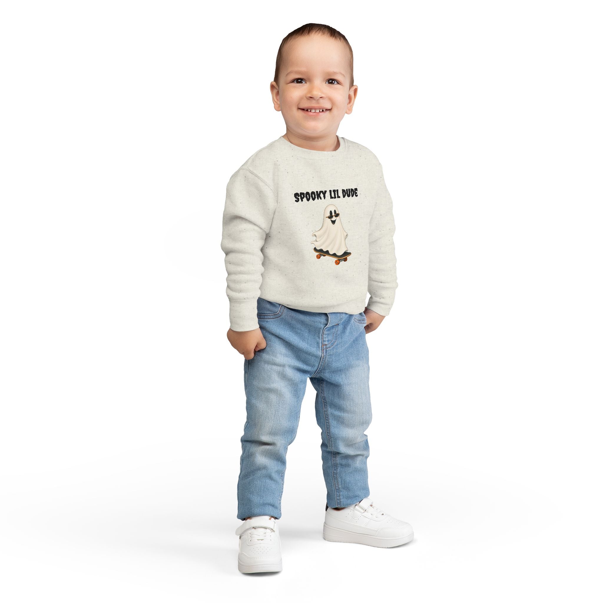 Toddler wearing a beige Spooky Lil Dude Halloween sweater featuring a cute ghost riding a skateboard, styled with casual jeans.